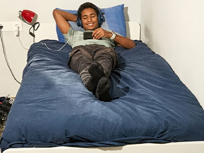 Young man with headphones using his phone while resting on a blue bed.