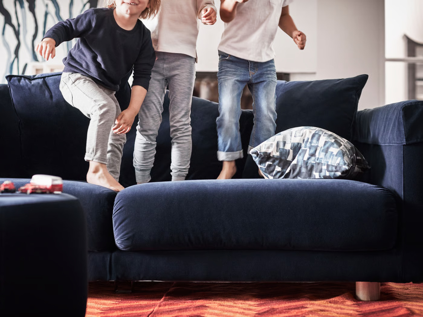 Three young children jumping playfully on a large navy blue sofa in a living room.